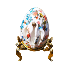 Sculpture d’une vulve sur un œuf précieux avec des motifs floraux bleus et oranges. Support en acier doré.